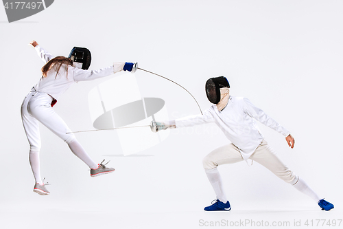 Image of The woman and man wearing fencing suit practicing with sword against gray