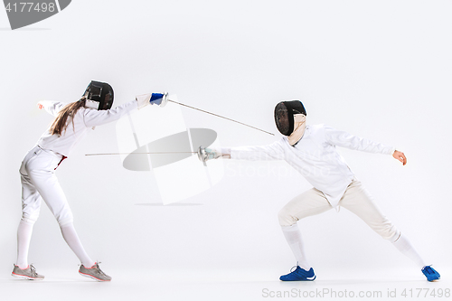 Image of The woman and man wearing fencing suit practicing with sword against gray