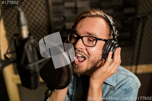 Image of man with headphones singing at recording studio