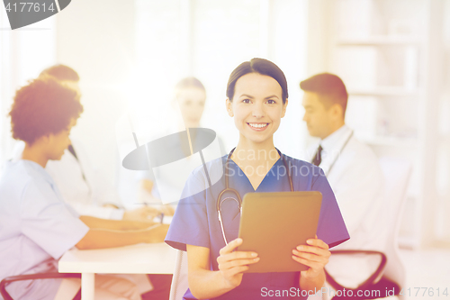 Image of happy doctor with tablet pc over team at clinic