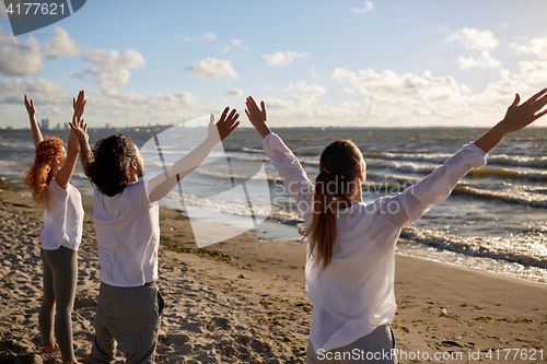 Image of group of people making yoga or meditating on beach