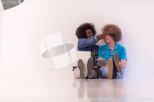 Image of multiethnic couple sitting on the floor with a laptop and tablet