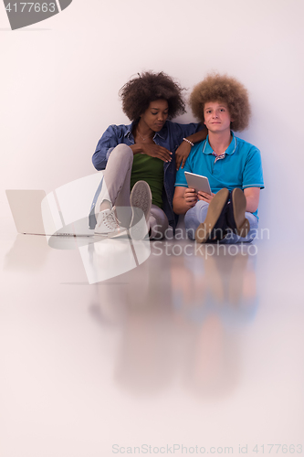 Image of multiethnic couple sitting on the floor with a laptop and tablet