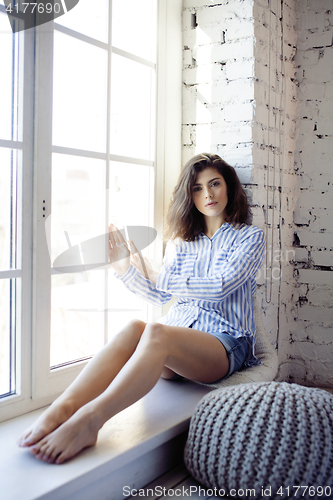 Image of young pretty brunette woman in her bedroom sitting at window, happy smiling lifestyle people concept