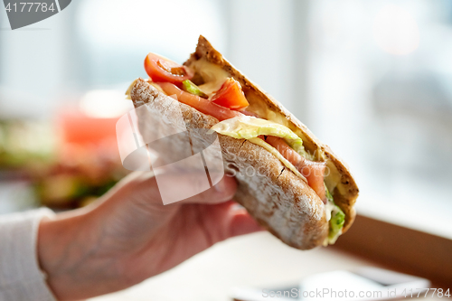 Image of hand with salmon panini sandwich at restaurant