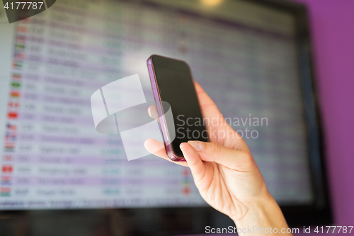 Image of hand with smartphone over exchange rates on screen