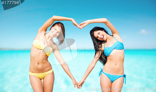 Image of happy women making heart shape on summer beach