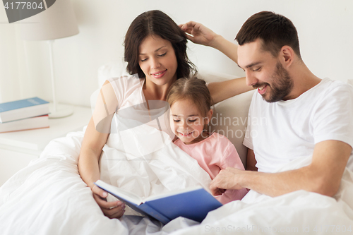 Image of happy family reading book in bed at home