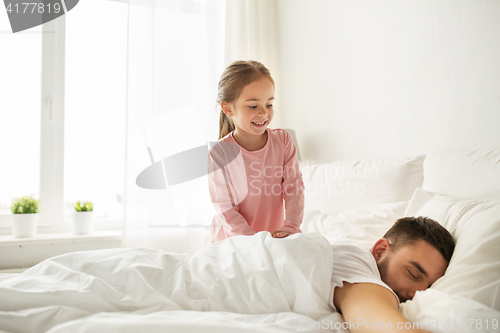 Image of little girl waking her sleeping father up in bed