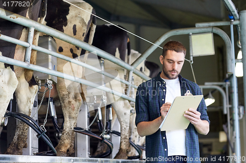 Image of man with clipboard and milking cows on dairy farm