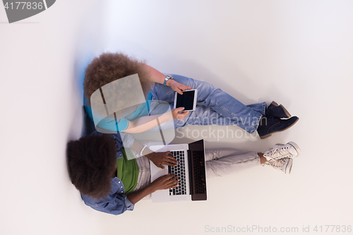 Image of multiethnic couple sitting on the floor with a laptop and tablet