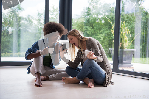 Image of multiethnic women sit on the floor and drinking coffee