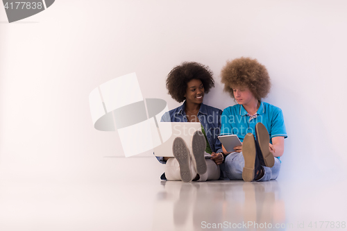 Image of multiethnic couple sitting on the floor with a laptop and tablet
