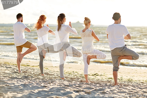 Image of group of people making yoga in tree pose on beach