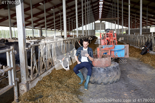 Image of young man with tablet pc and cows on dairy farm