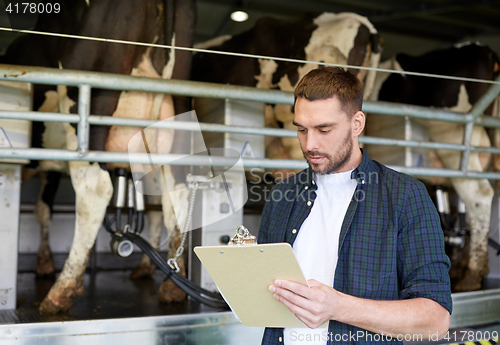 Image of man with clipboard and milking cows on dairy farm