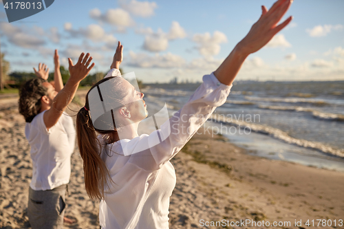 Image of group of people making yoga or meditating on beach