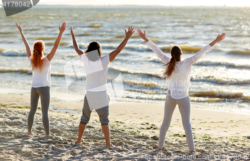 Image of group of people making yoga or meditating on beach