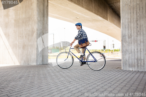 Image of young hipster man with bag riding fixed gear bike