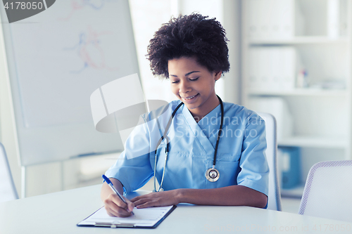 Image of happy female doctor or nurse writing to clipboard