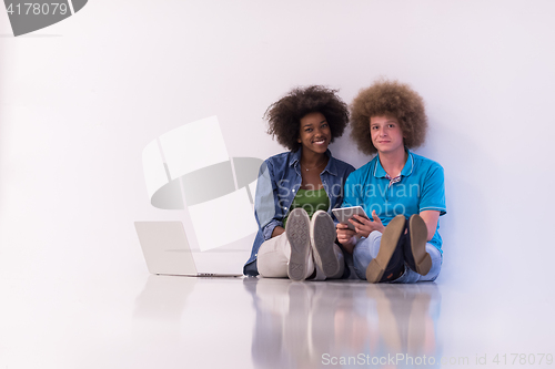 Image of multiethnic couple sitting on the floor with a laptop and tablet