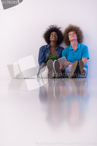 Image of multiethnic couple sitting on the floor with a laptop and tablet