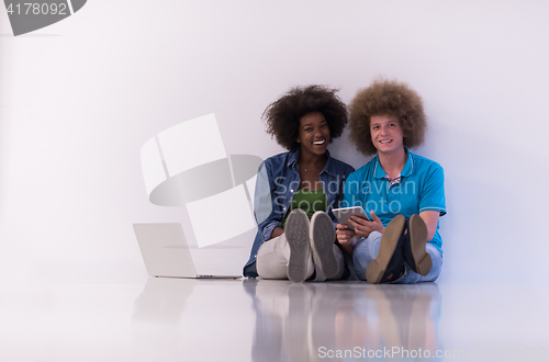 Image of multiethnic couple sitting on the floor with a laptop and tablet