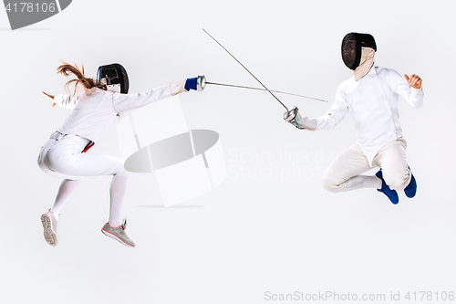 Image of The woman and man wearing fencing suit practicing with sword against gray