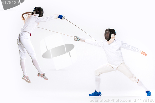 Image of The woman and man wearing fencing suit practicing with sword against gray