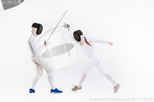 Image of The woman and man wearing fencing suit practicing with sword against gray