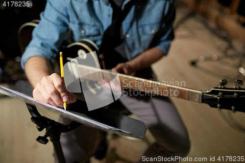 Image of man with guitar writing to music book at studio