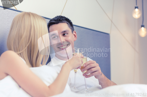 Image of smiling couple with champagne glasses in bed