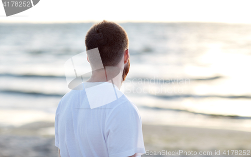 Image of young man in white t-shirt on beach looking at sea