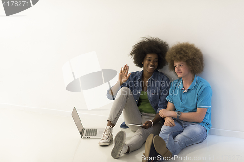 Image of multiethnic couple sitting on the floor with a laptop and tablet