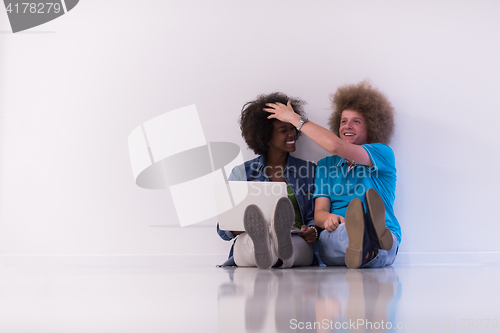 Image of multiethnic couple sitting on the floor with a laptop and tablet