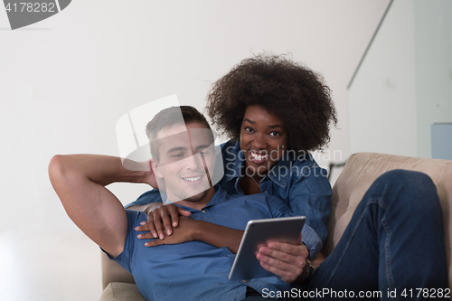 Image of multiethnic couple relaxing at  home with tablet computers