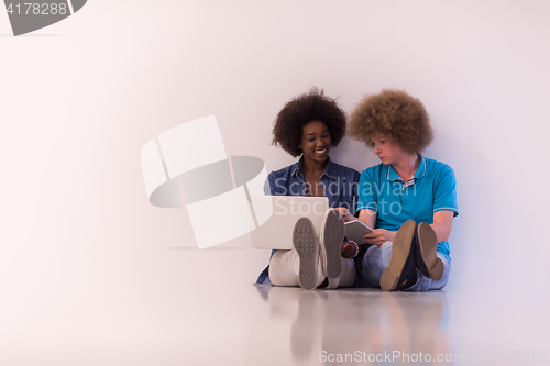Image of multiethnic couple sitting on the floor with a laptop and tablet