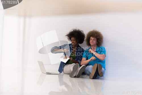 Image of multiethnic couple sitting on the floor with a laptop and tablet