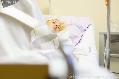 Image of Bedridden female patient recovering after surgery in hospital care.