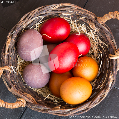 Image of Wicker basket with colorful Easter eggs on wooden table.
