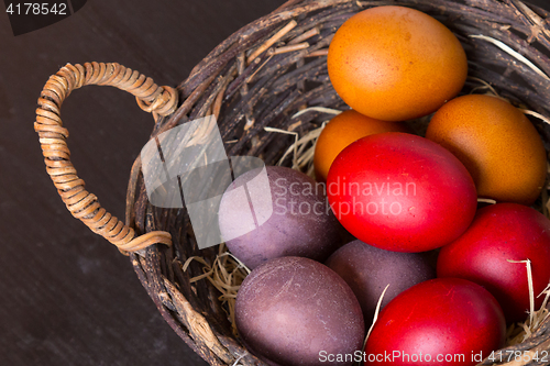 Image of Wicker basket with colorful Easter eggs on wooden table.