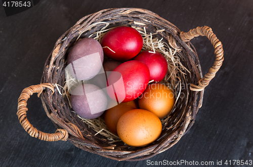 Image of Wicker basket with colorful Easter eggs on wooden table.