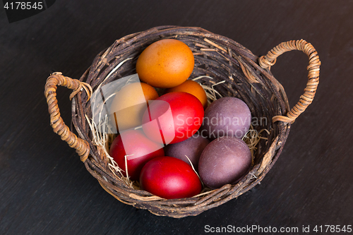 Image of Wicker basket with colorful Easter eggs on wooden table.