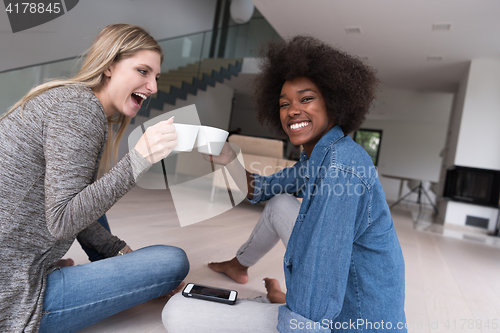 Image of young multiethnic women sit on the floor and drinking coffee