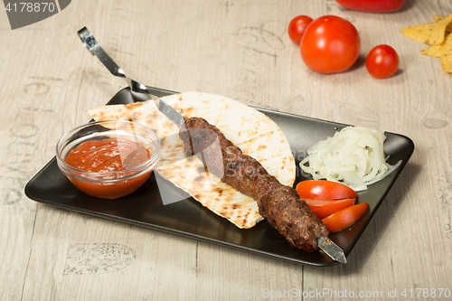 Image of shashlik. kebab skewer, black rectangular plate. sauce and onions