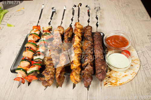 Image of set shashlik. kebab skewer, black rectangular plate. sauce and onions