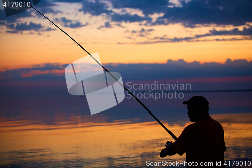 Image of Silhouette of fishermen on quiet ocean with rays sunset