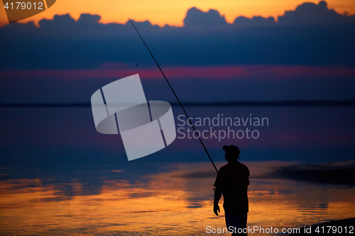 Image of Silhouette of fishermen on quiet ocean with rays sunset