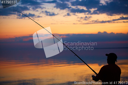 Image of Silhouette of fishermen on quiet ocean with rays sunset