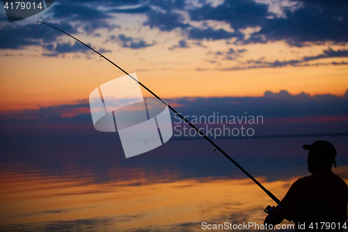 Image of Silhouette of fishermen on quiet ocean with rays sunset